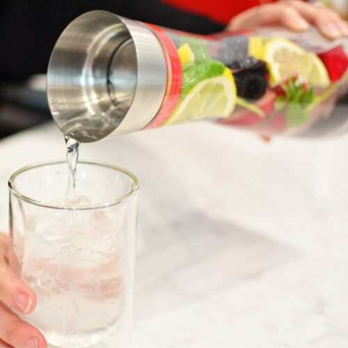 Grosche-rio-water-and-fruit-infuser-being-held-on-white-marble-counter-and-pouring-water-into-glass